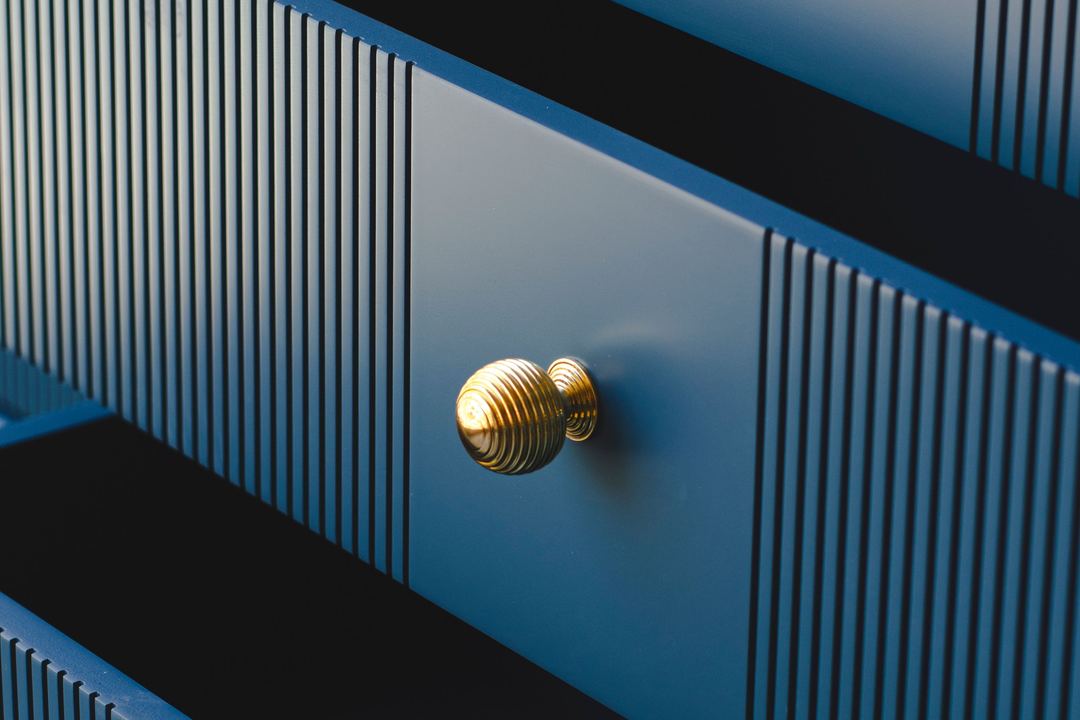 Gerippte Messingknöpfe an den Schubladen eines blauen, gestreiften Sideboards.